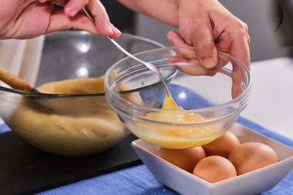 Volcar la masa a un bol, para cortar la cocción, y empezar a añadir los huevos, de uno en uno, y ya batidos