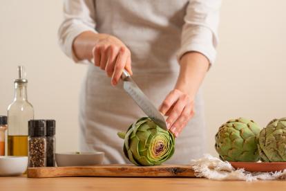 Un cocinero parte con un cuchillo una alcachofa.
